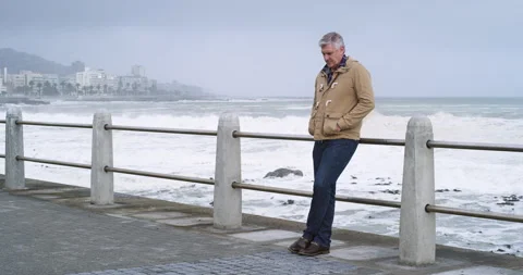 Thinking, thoughtful and concerned senior man standing near the beach on a cold Stock Footage