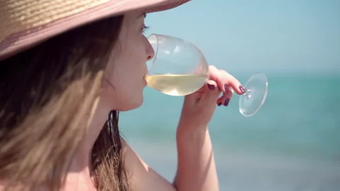 Thinking woman in summer hat drinking refreshing white wine at the sea beach Stock Footage 159275035