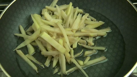 Thinly cut potatoes added to hot oil in frying pan on stovetop Stock Footage 146888665