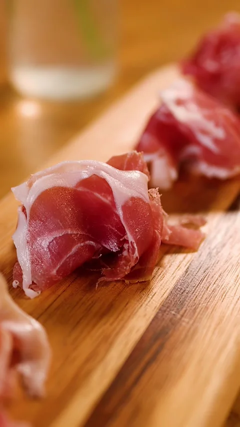 Thinly Sliced Cured Ham Appetizer Served on a Wooden Board Stock Footage 337917702