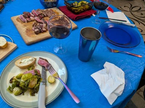Thinly sliced steak served with bread, brussels sprouts, wine, and utensils Stock Photos