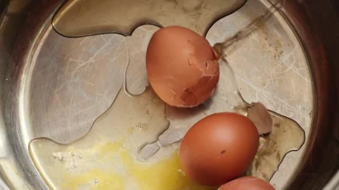 A third raw brown chicken egg falls into a metal pot containing broken shel.. Stock Footage 344112416