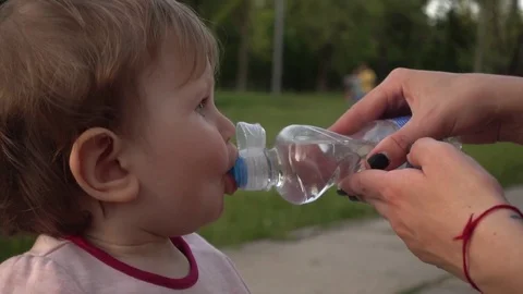 Thirsty Child Drinking Water On Bench In Park, Sitting with Mom Stock Footage 75253933