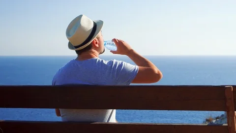 Thirsty man relax on bench at edge of cliff drink water from plastic bottle Stock Footage 98609524