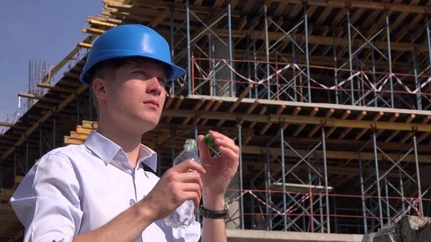 Thirsty young engineer lunch with helmet builder drinking water at building site Stock Footage
