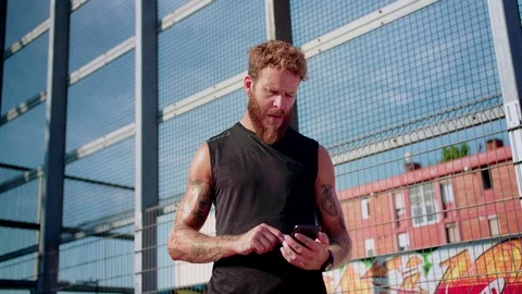 Thoughtful alluring bearded guy using holding in tattooed arms black smartphone Stock Footage 116740428