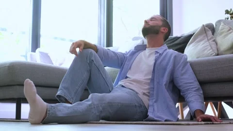 Thoughtful and depressed bearded man sitting alone on the living room floor Stock Footage 344757144