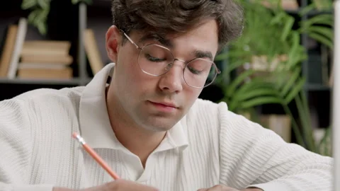 Thoughtful and smiling student at desk, participating in online classes. Young Stock Footage 316090923