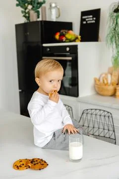 Thoughtful, angry boy eats breakfast cookies and milk and looks at the camera Stock Photos