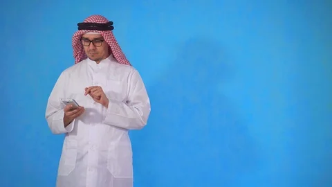Thoughtful arab man standing on a blue background uses the phone Video stock 107345889