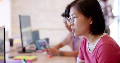 Thoughtful asian female creative working at computer in casual office, slow Stock Footage 335682546