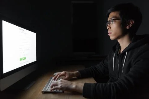 Thoughtful asian man using computer at table in dark room Stock Photos