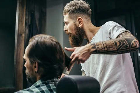 Thoughtful barber looking at the mirror while touching hair of client Foto stock