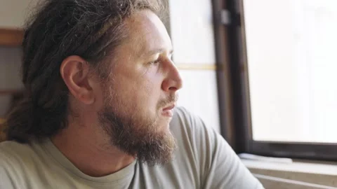 Thoughtful bearded man eating and looking out a window Stock Footage 320057794