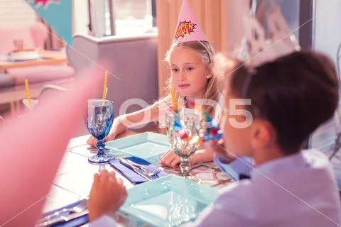 Thoughtful birthday girl wearing party hat and looking at the table Stock Photos