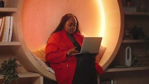 Thoughtful Black female AI developer works on laptop in modern library Stock Footage 343435928