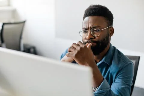 Thoughtful black man in eyeglasses stack with hard task, looking at computer Foto stock