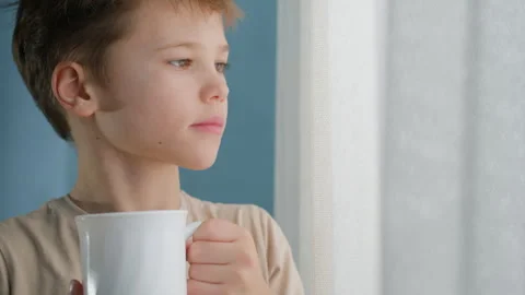 Thoughtful boy holding white ceramic mug of hot tea or cocoa. Stock Footage 328479828