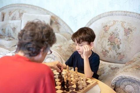 Thoughtful boy playing chess with elderly woman Stock Photos