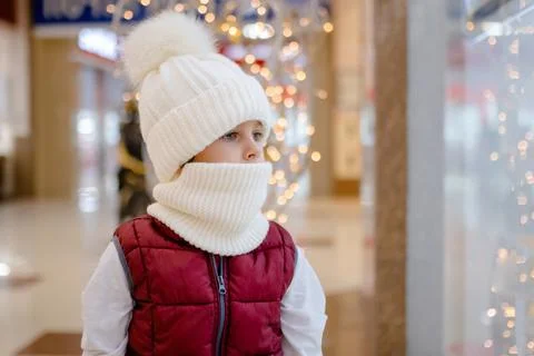 Thoughtful boy in white bobble hat and scarf at mall near showcase. blurred Stock Photos