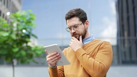 Thoughtful businessman is using digital tablet while standing on street near  Stock Footage 308100380