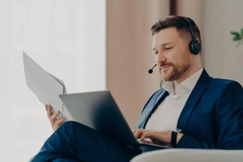 Thoughtful businessman working with online project at home while holding papers Foto stock