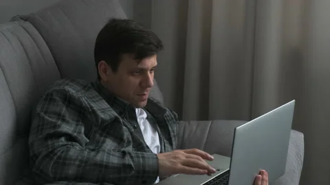 Thoughtful calm man is lying on comfortable couch working remotely on laptop. Stock Footage 154157262