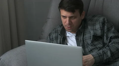 Thoughtful calm man is lying on comfortable couch working remotely on laptop. Video stock 158805157