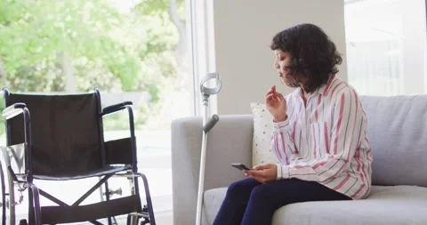 Thoughtful disabled woman using smartphone in living room, crutch and wheelchair Stock-Footage 344849454