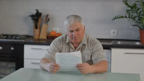 Thoughtful Elderly Gentleman Reviewing Document in His Home Kitchen Stock Footage 327911493