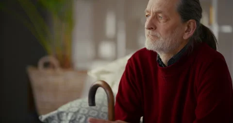 Thoughtful elderly man sitting in profile with walking cane at home Stockbeeldmateriaal 336278389