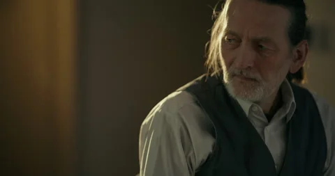 Thoughtful elderly man standing in warm dim indoor light Видео 336279402