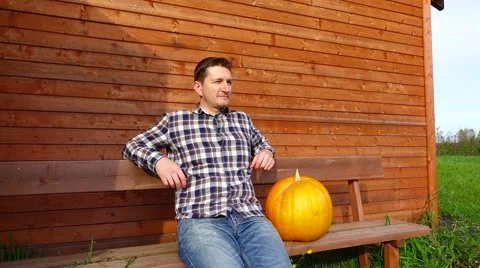 Thoughtful farmer sit on a bench with big pumpkin, look at distance Stock Footage