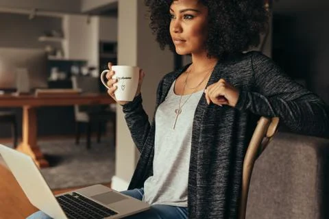 Thoughtful female having coffee while working on laptop at home Stock Photos