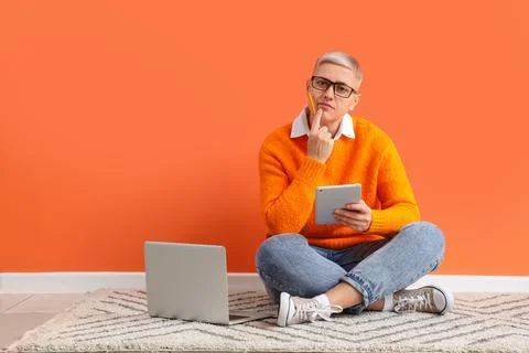 Thoughtful female programmer with tablet computer and laptop sitting near ora Stock Photos