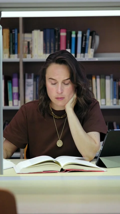 Thoughtful Female Student Reading a Book and Writing in a Library Stock Footage 336041973