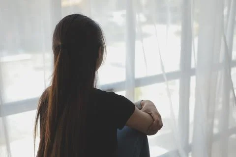 Thoughtful girl sitting on sill embracing knees looking at window, sad depr.. Stock Photos