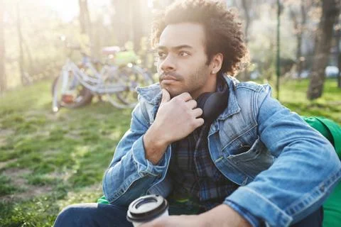 Thoughtful handsome dark-skinned guy with bristle touching chin while sitting on 스톡 사진