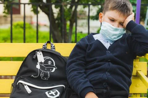 Thoughtful kid boy in mask thinking. a sad schoolboy looking sitting on a ben Stock Photos