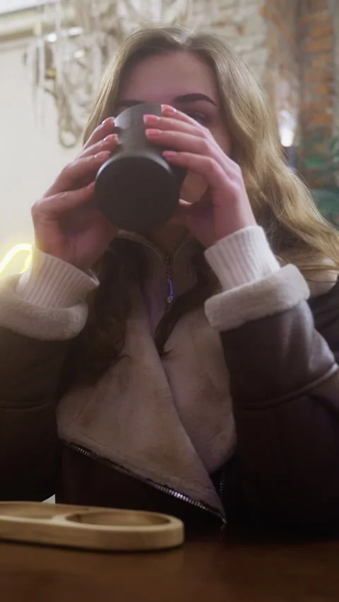 Thoughtful lady in brown shearling jacket sipping coffee in cozy caf with soft Video stock 320357759
