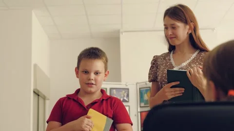 Thoughtful little boy talks about book standing by teacher in extended day group Stock Footage 249900533