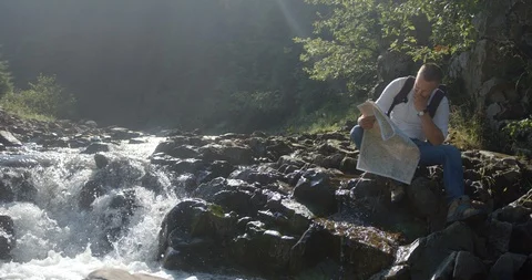The thoughtful lost hiker man is looking for the way using paper map and sitting Stock Footage 87798520