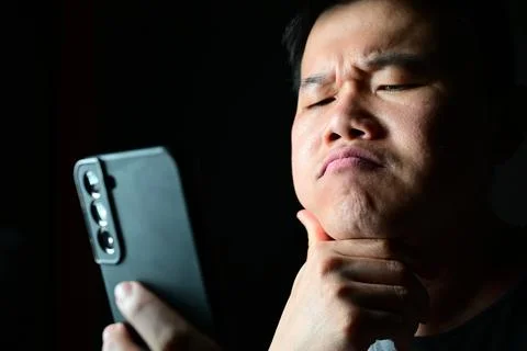 Thoughtful man analyzing smartphone content with thinking expression 스톡 사진