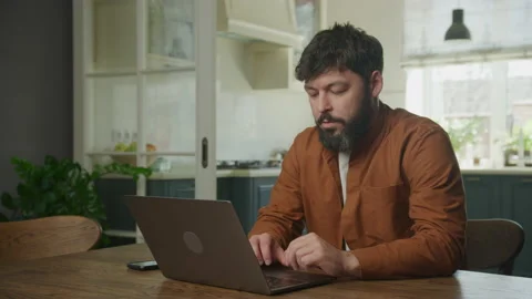 Thoughtful man browsing and working on his laptop in his apartment 動画素材 195978575