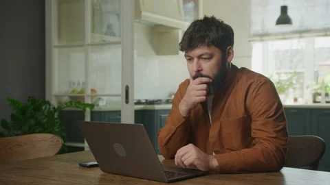 Thoughtful man browsing and working on his laptop in his apartment Stockbeeldmateriaal 199248844