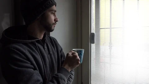 Thoughtful Man with a Cap Drinks Cup of Coffee near a Window Stock Footage 72099717