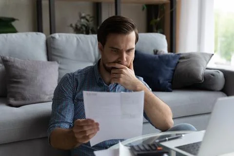 Thoughtful man checking financial documents, calculating bills, using laptop Fotos de archivo