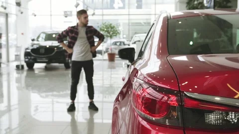 Thoughtful man contemplating his next car purchase at a sleek dealership Stock Footage 311982787
