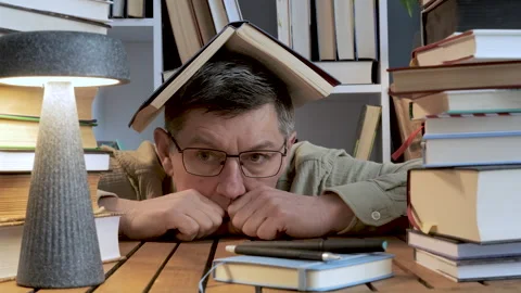 Thoughtful Man Holding Book Above Head Among Book Stacks Stock Footage 346062890