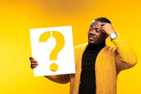 Thoughtful man holding a question mark sign against a yellow background Stock Photos
